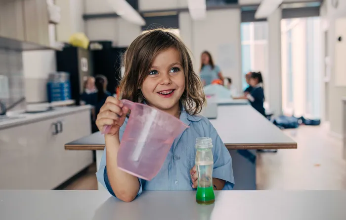 A child in school pouring into a volcano and smiling