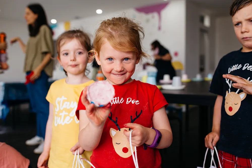 A child holding a bath bomb and smiling at the camera