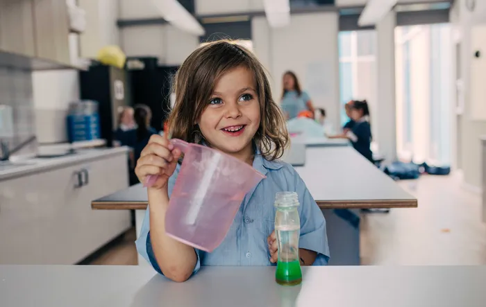A child in school pouring into a volcano and smiling
