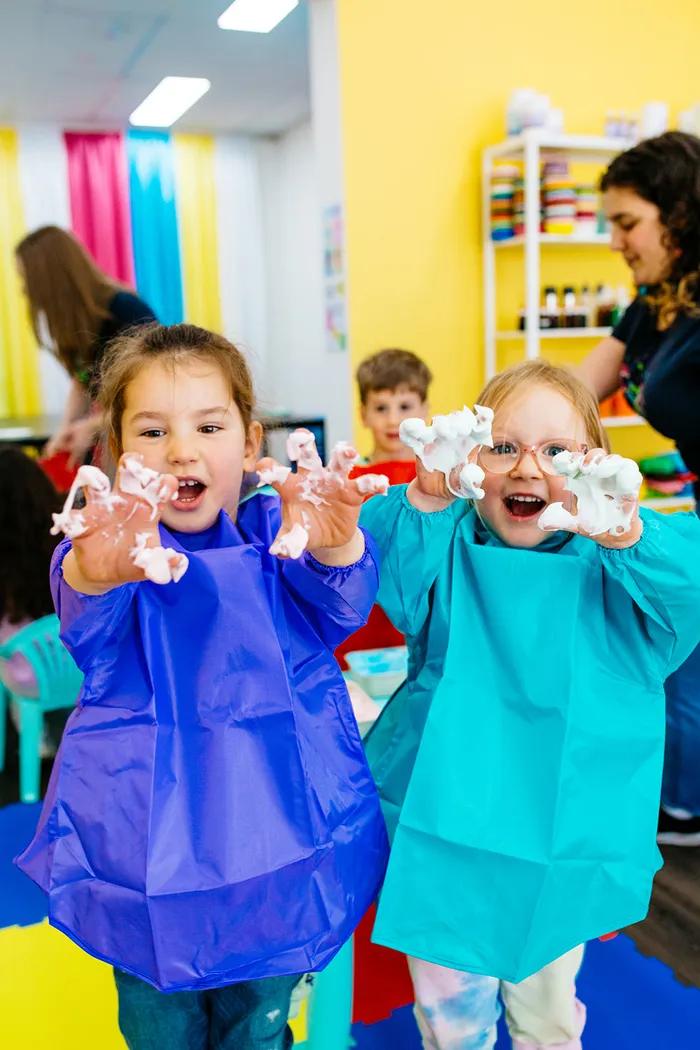 Two kids in aprons showing off their messy hands